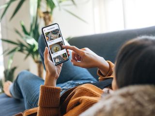 Woman choosing food from the menu on mobile app while lying on the couch at home
