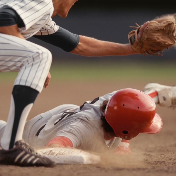 Base runner sliding into base while fielder catches a ball in baseball game