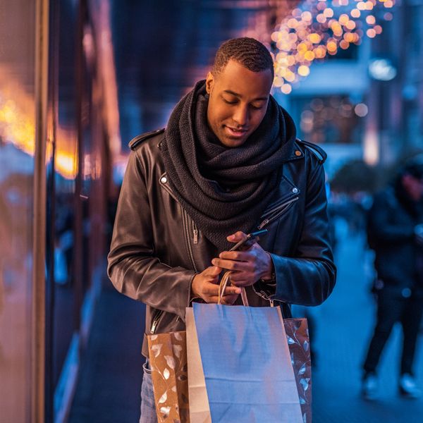 Man wearing winter clothes standing on a street holding paper bags and using a smartphone