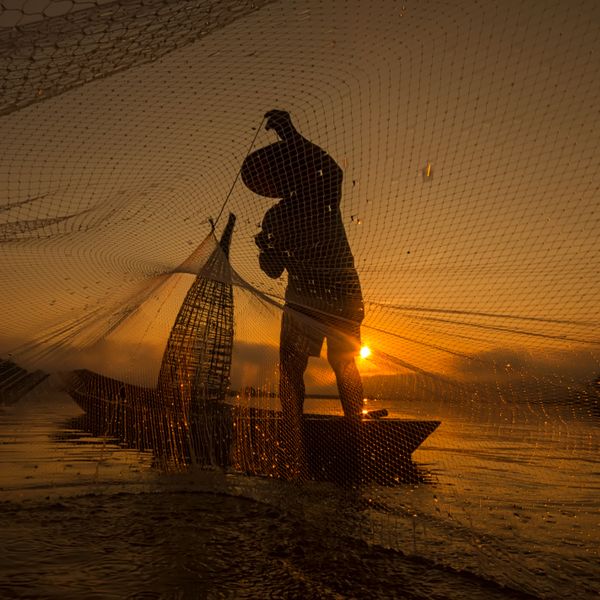 Silhouette of fishing boat and fisherman on sunset