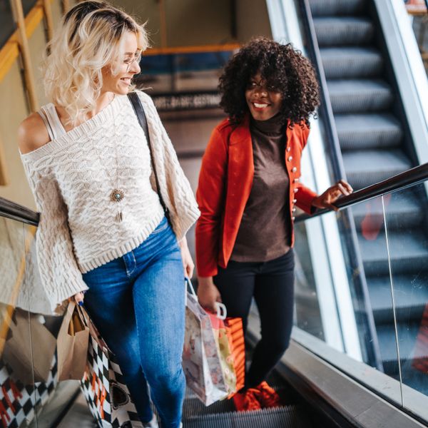 Two women looking at each other and smiling while on a scalator at a shopping center