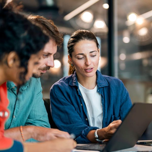 A diverse team of colleagues reviewing a project on a laptop in a modern office.