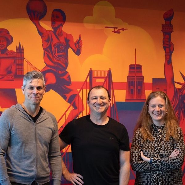 CI&T founders Bruno Guicardi and Cesar Gon with EMEA director Carolina Wosiack smiling and standing in front of a mural